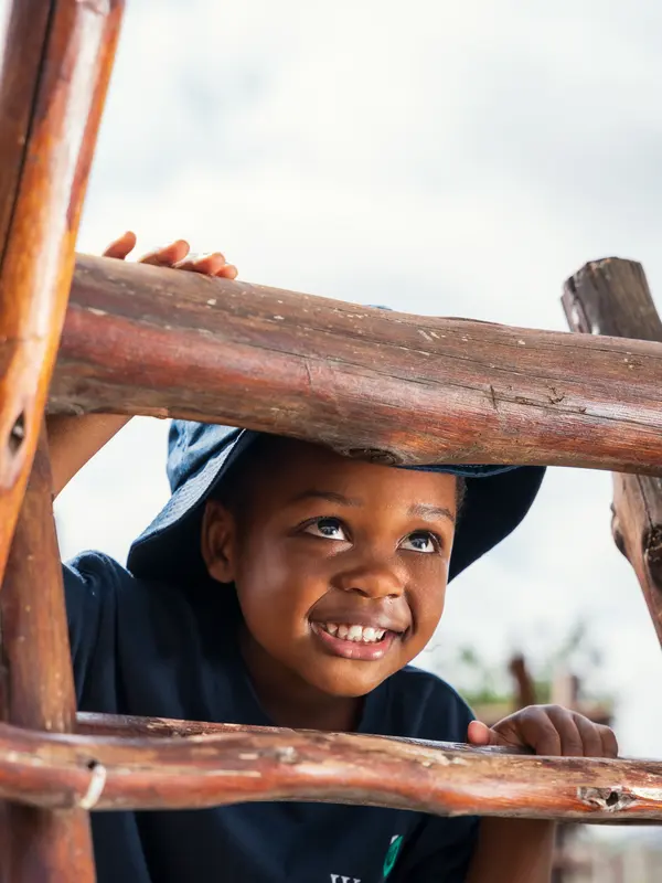 A child smiling from inside a wooden play structure