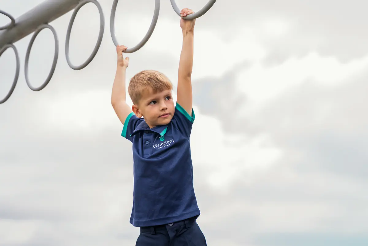A child swinging from playground rings against the sky