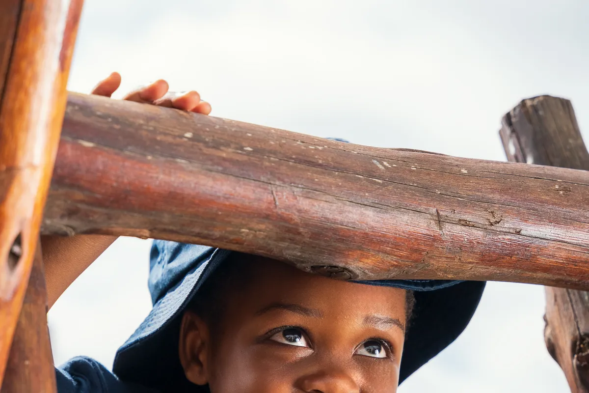 A child smiling from inside a wooden play structure