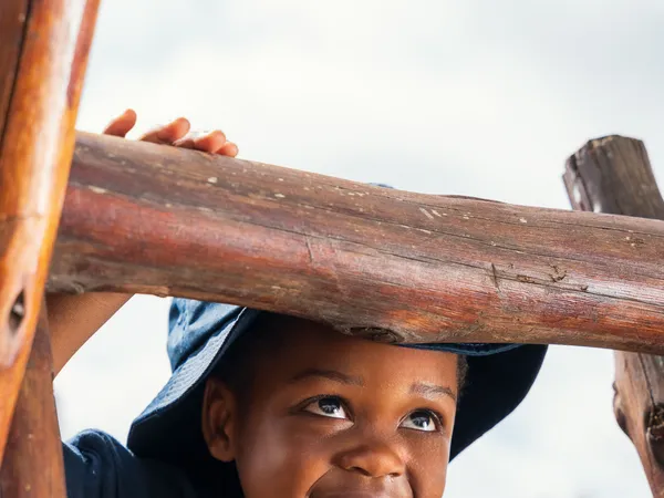 A child smiling from inside a wooden play structure