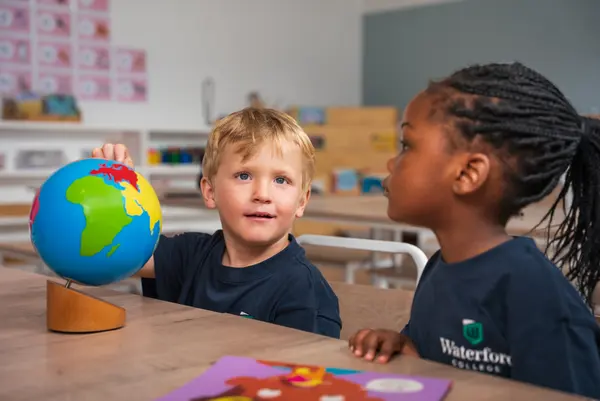 Two children talking across a table with a globe